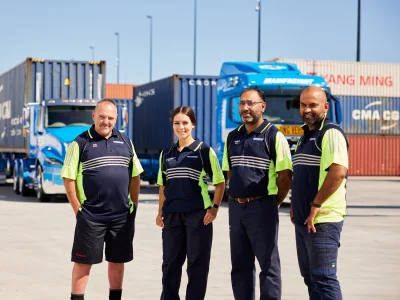 Four Mainfreight team members standing in front of two Wharf Cartage Trucks
